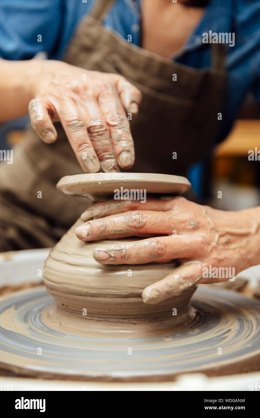 Hands of senior female potter working on pottery wheel while sitting in ...