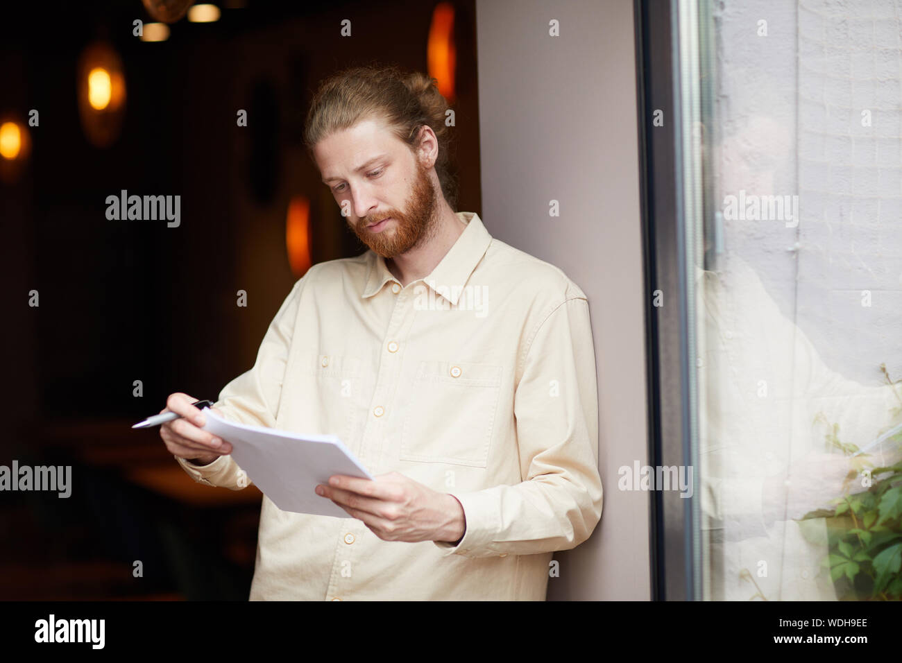 Young bearded man holding documents reading and checking it while standing outdoors Stock Photo