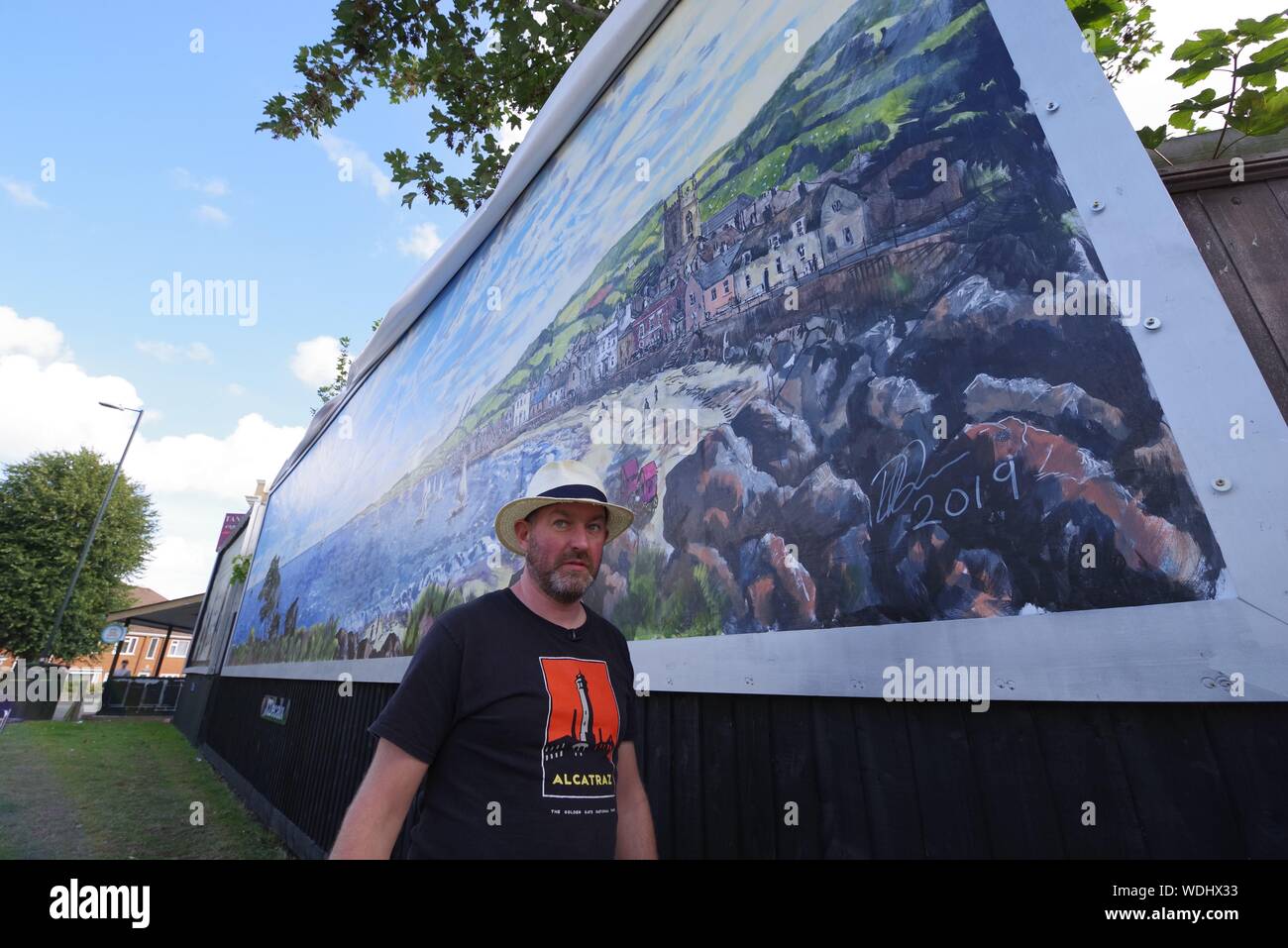 British artist David Downes has been commissioned by ITV to create a large-scale public mural in Bournemouth in conjunction with the  launch of their 2019 drama Sanditon in August 2019. Painting publicly for 5 days, and here on day 5, Downes is recreating an illustrated version of the poster artwork for Sanditon, on a giant billboard in the UK’s coastal town, to reﬂect the seaside location of the drama. The installation will remain in situ for three weeks after its completion.   David Downes is a landscape painter who ampliﬁes the sense of place and time through the lens of autism. Stock Photo