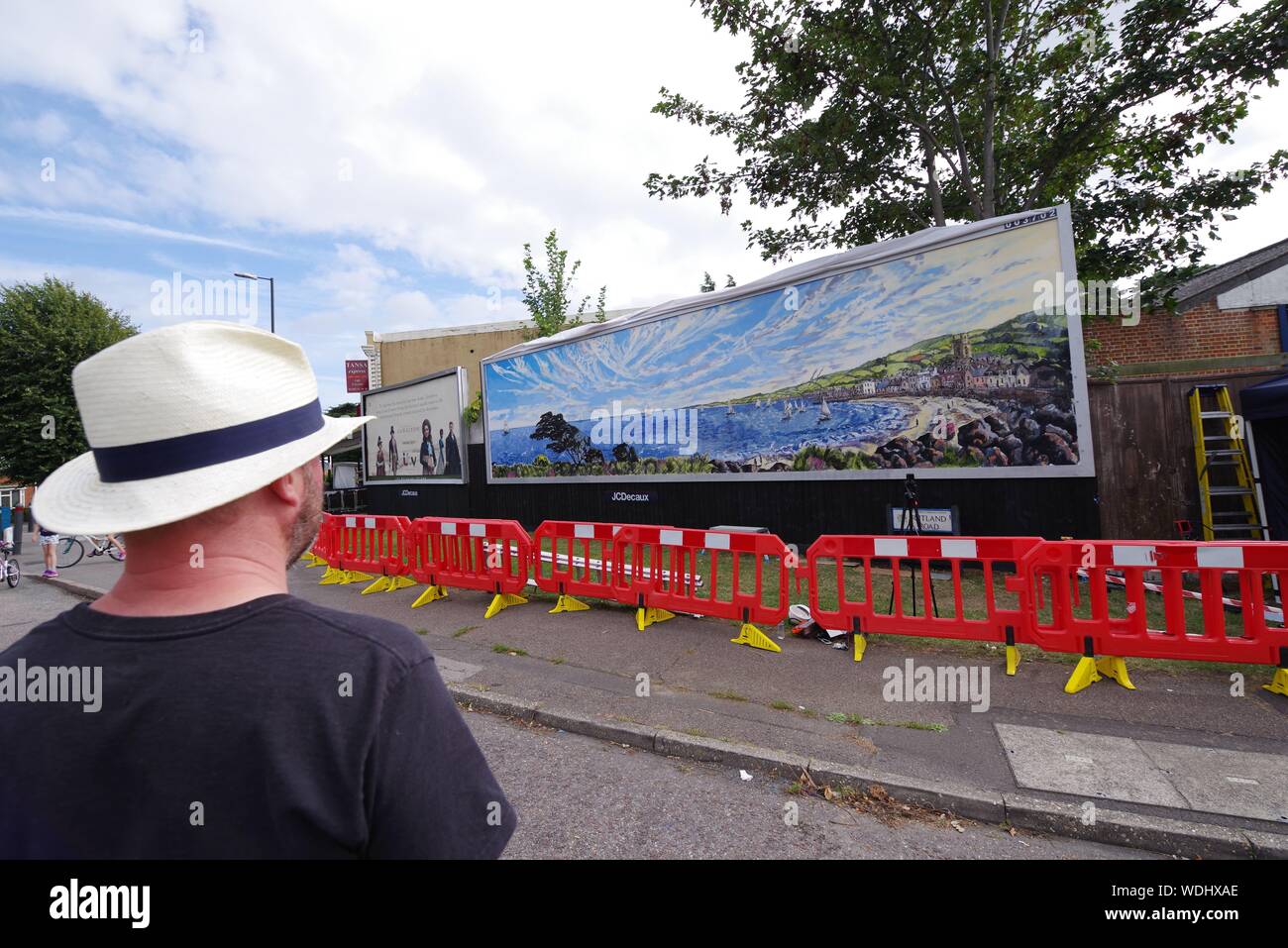British artist David Downes has been commissioned by ITV to create a large-scale public mural in Bournemouth in conjunction with the  launch of their 2019 drama Sanditon in August 2019. Painting publicly for 5 days, and here on day 5, Downes is recreating an illustrated version of the poster artwork for Sanditon, on a giant billboard in the UK’s coastal town, to reﬂect the seaside location of the drama. The installation will remain in situ for three weeks after its completion.   David Downes is a landscape painter who ampliﬁes the sense of place and time through the lens of autism. Stock Photo