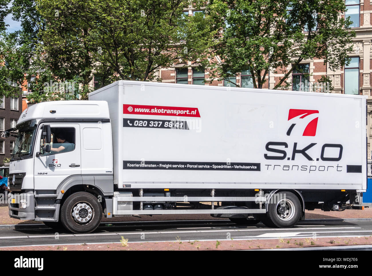 Amsterdam, the Netherlands - June 30, 2019: Large white transport truck with black red lettering for S.K.O. company. Green foliage above. Brown-wh Stock Photo - Alamy