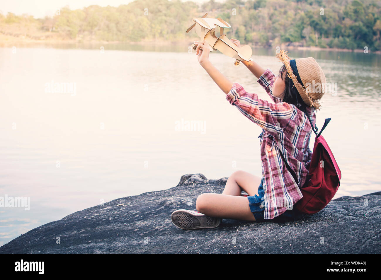 Side View Of Girl Holding Wooden Airplane On Rock By Lake Stock Photo