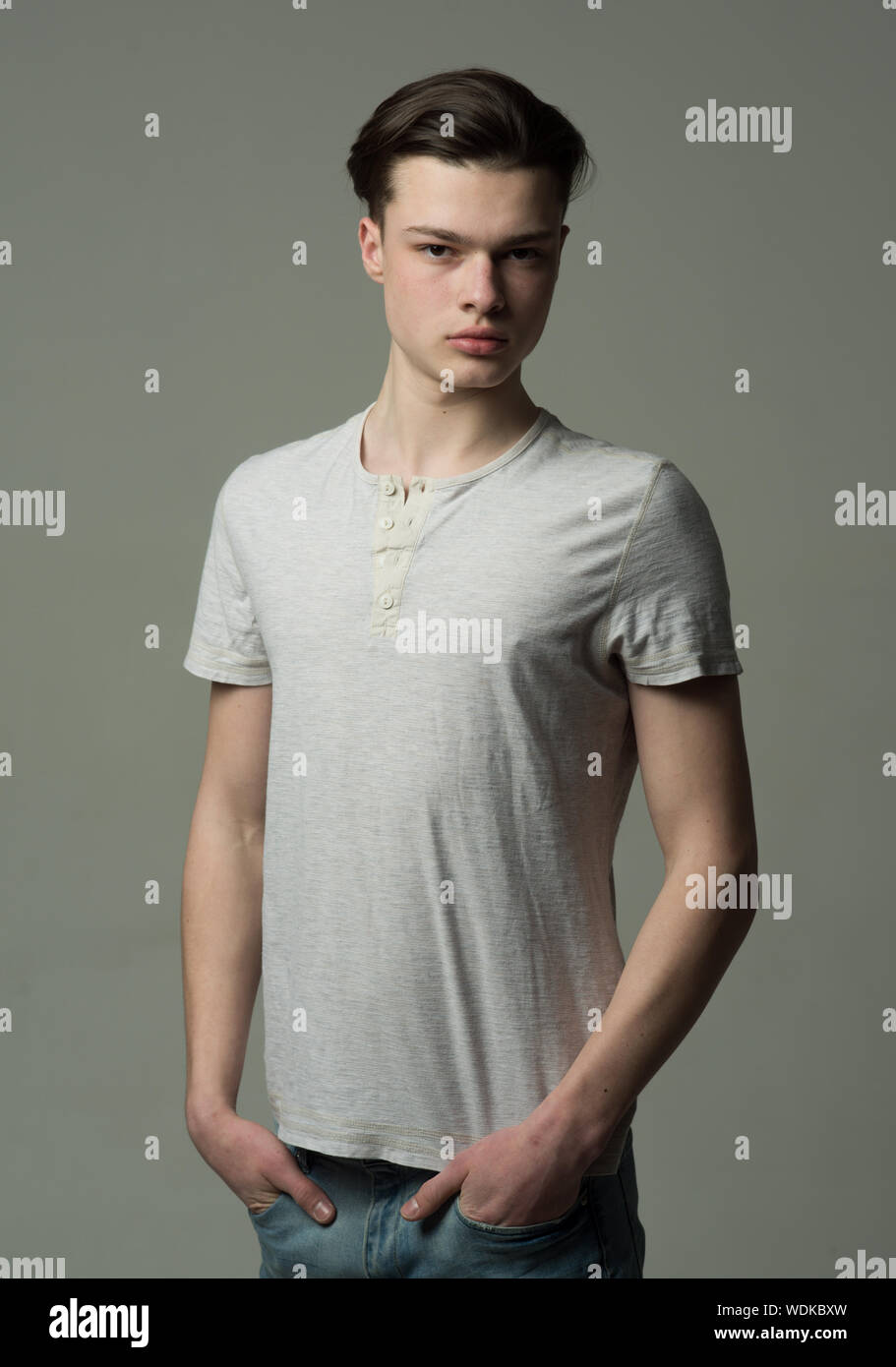 Studio portrait of a serious brunette young man with medium length hair  isolated on gray background. Handsome teenage boy in white T-shirt and blue  je Stock Photo - Alamy, image size:911x1390
