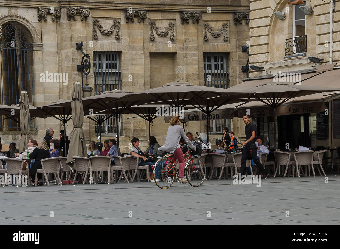 Woman riding a bike in front of a terrace at Place Pey Berland, in the city of Bordeaux, France, in September 2013 Stock Photo