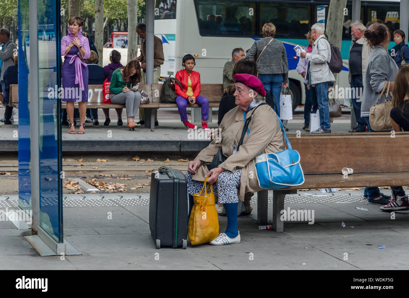 Lady with suitcases and bags waits for the bus sitting in the city of Bordeaux, France, in September 2013 Stock Photo