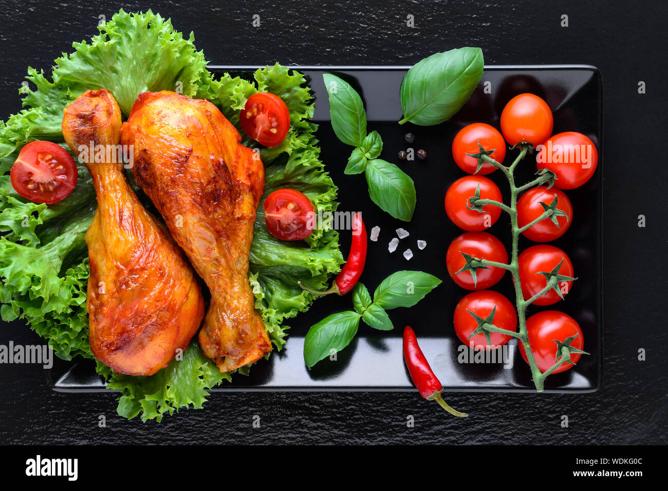 healthy grilled chicken legs with fresh tomato, basilik and chili on black background Stock Photo
