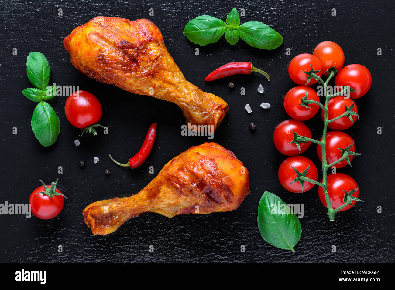 healthy grilled chicken legs with fresh tomato, basilik and chili on black background Stock Photo