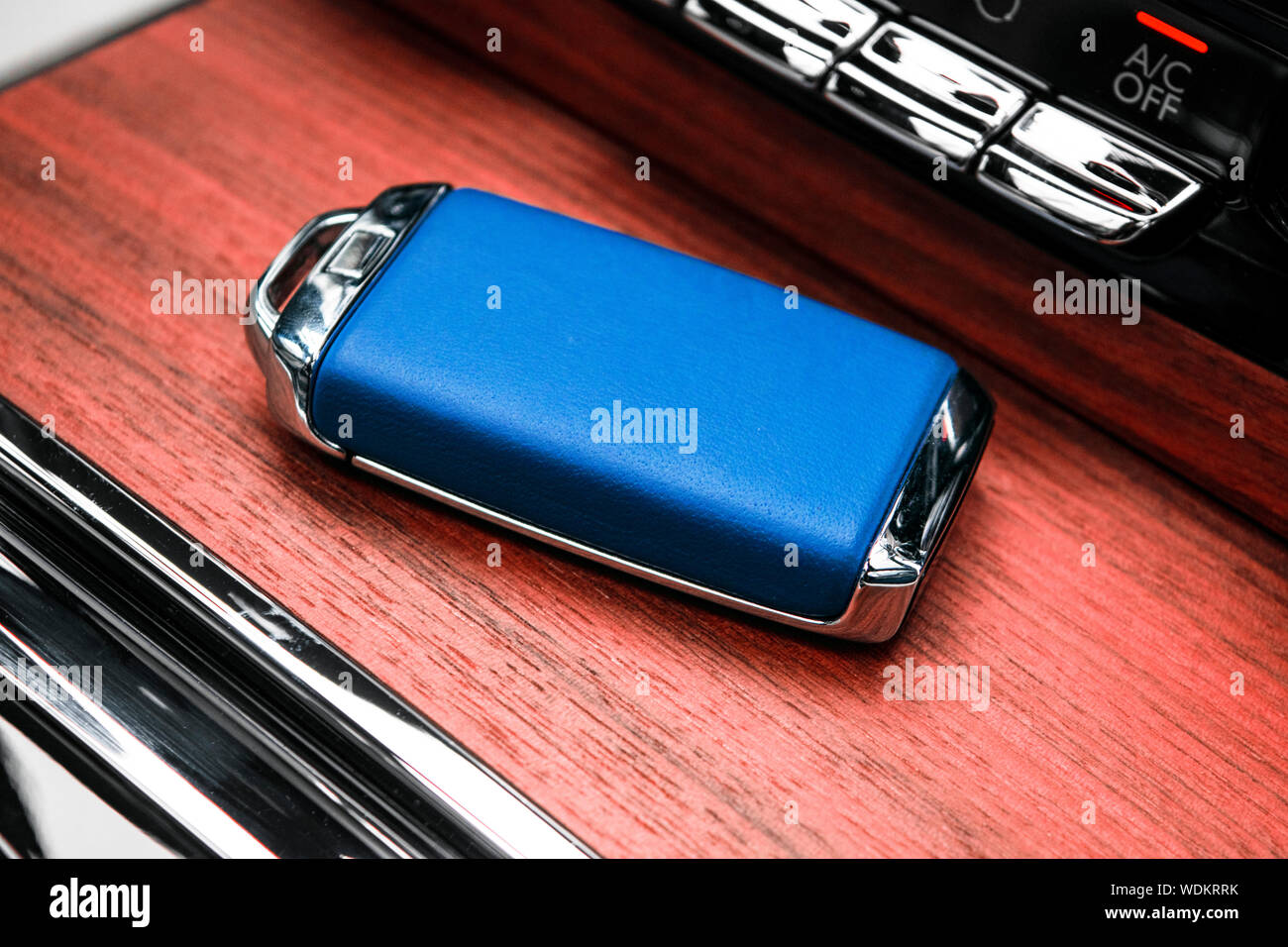 Closeup inside vehicle of wireless blue leather key ignition on natural wood panel. Wireless start engine key. Car key remote isolated. Modern Car key Stock Photo