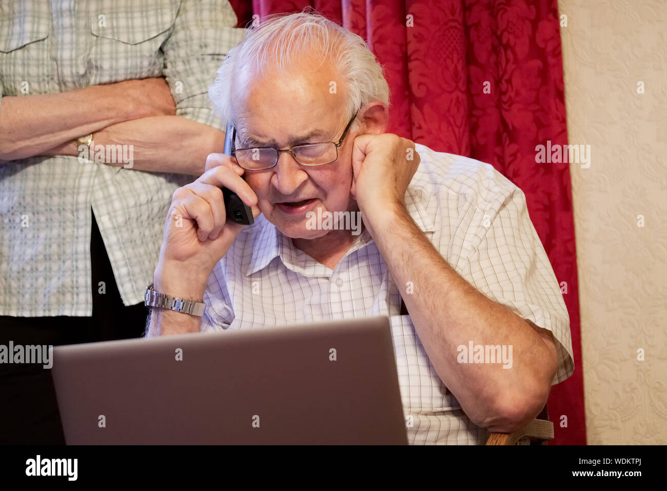Old elderly senior man on phone at laptop computer at risk to cyber attack and online bank fraud Stock Photo