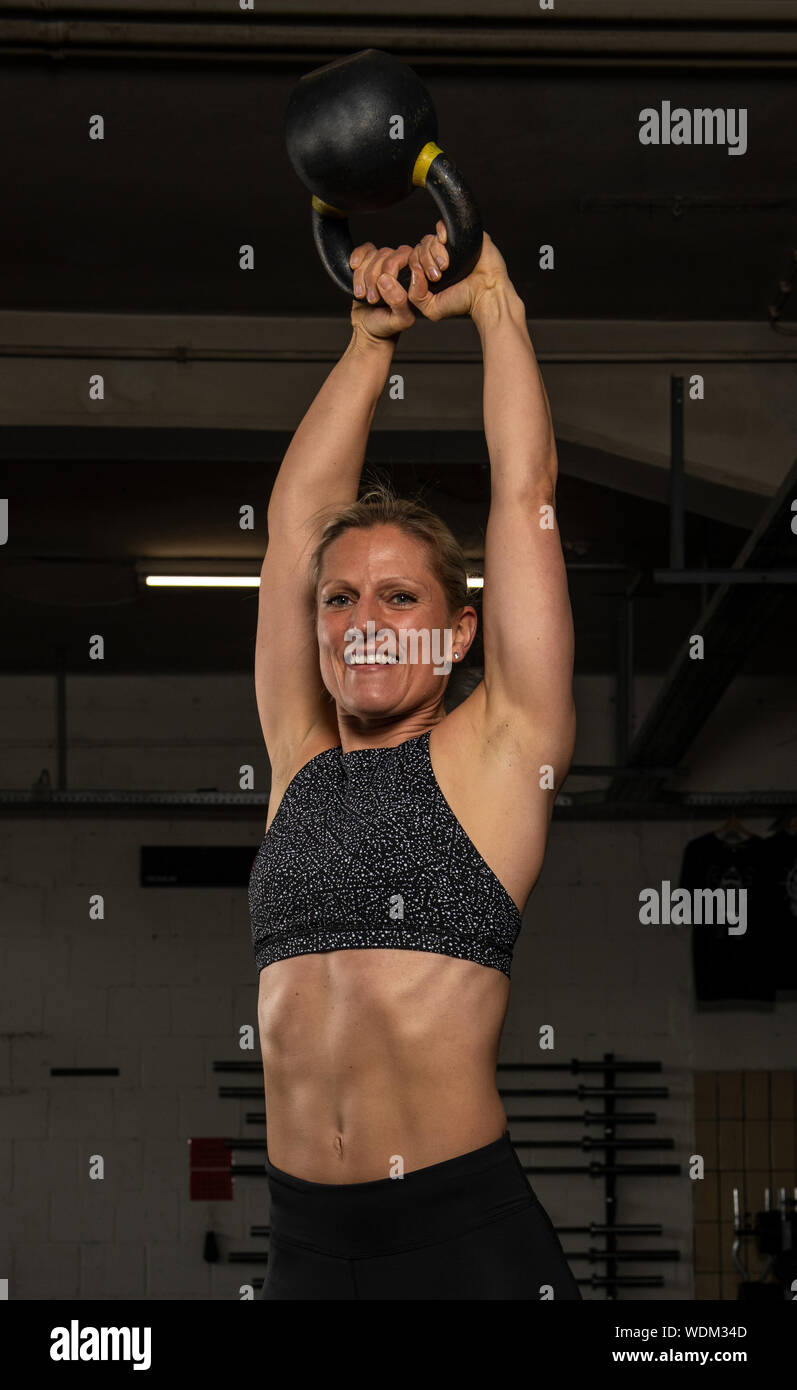 An attractive middle aged woman with strong abs is doing kettlebell swings. The beautiful athlete is doing a functional fitness workout in a gym. Stock Photo