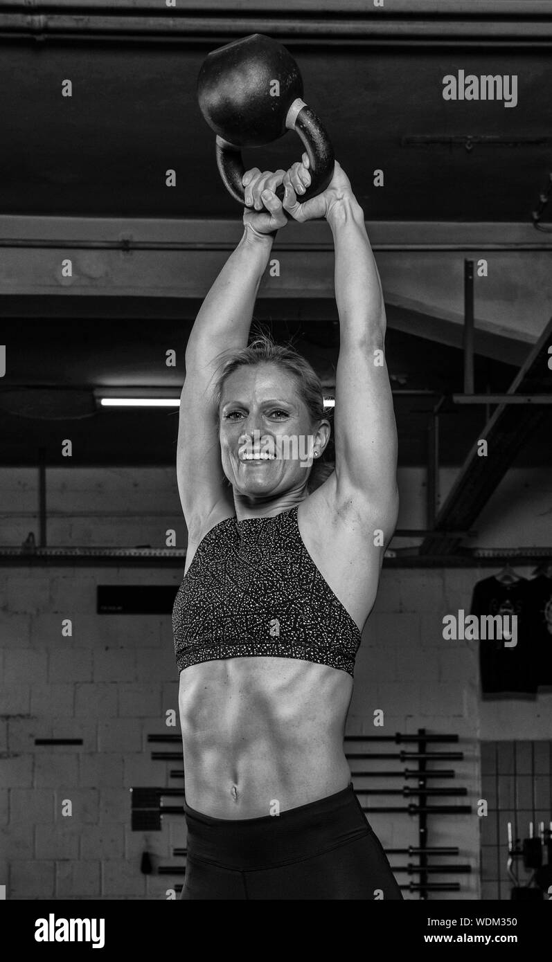 An attractive middle aged woman with strong abs is doing kettlebell swings. The beautiful athlete is doing a functional fitness workout in a gym. Stock Photo