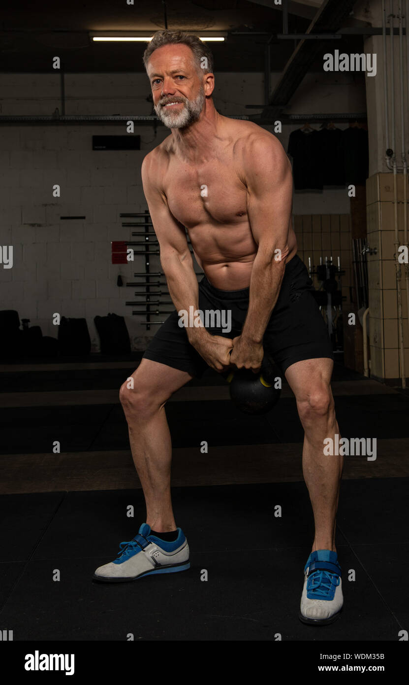 An attractive middle aged man with strong abs is doing kettlebell