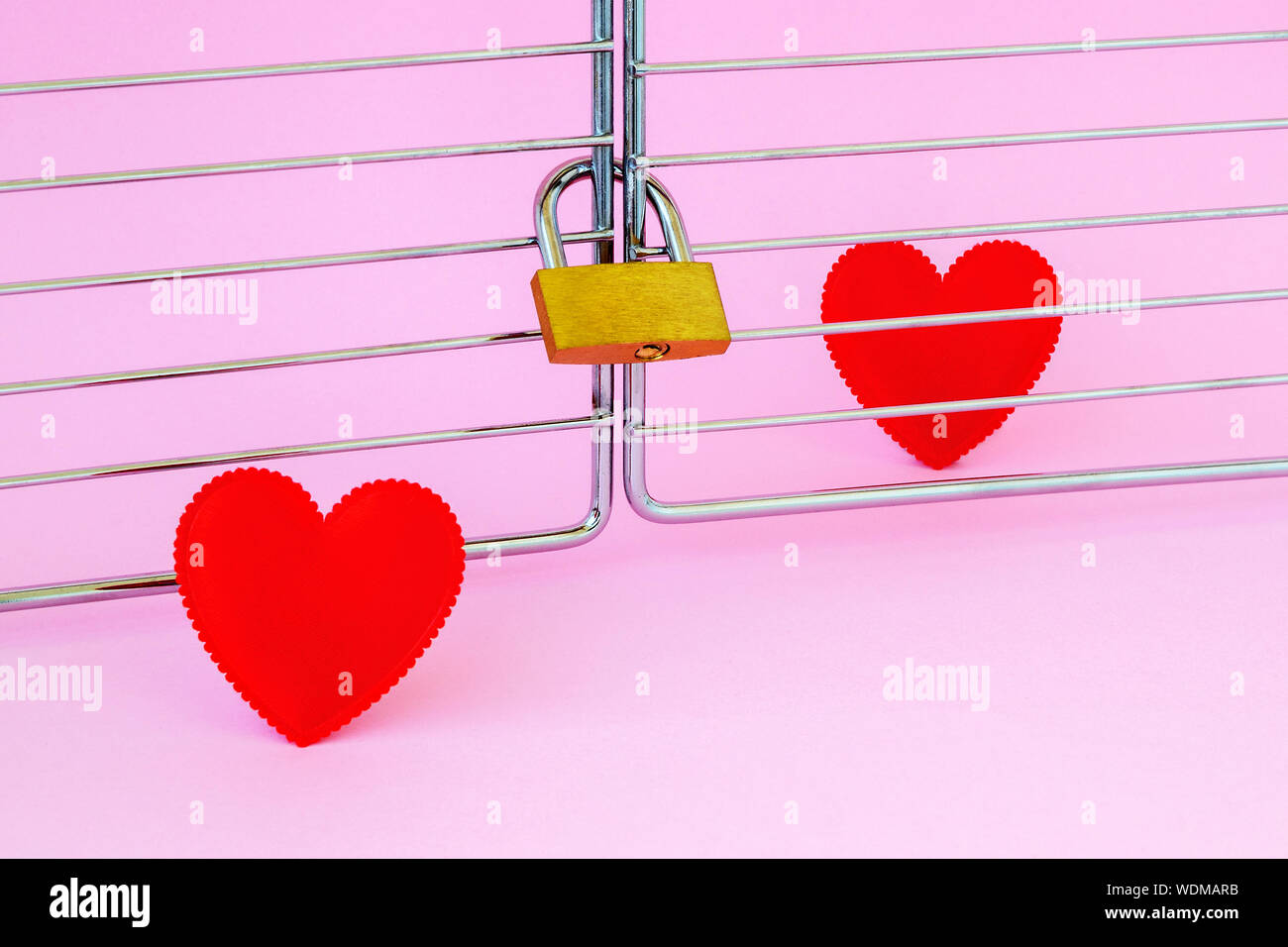 One red silk heart is in a cage locked with padlock and another one is outside. To meet a heartmate and to open heart for soulmate consepts. On a pink Stock Photo