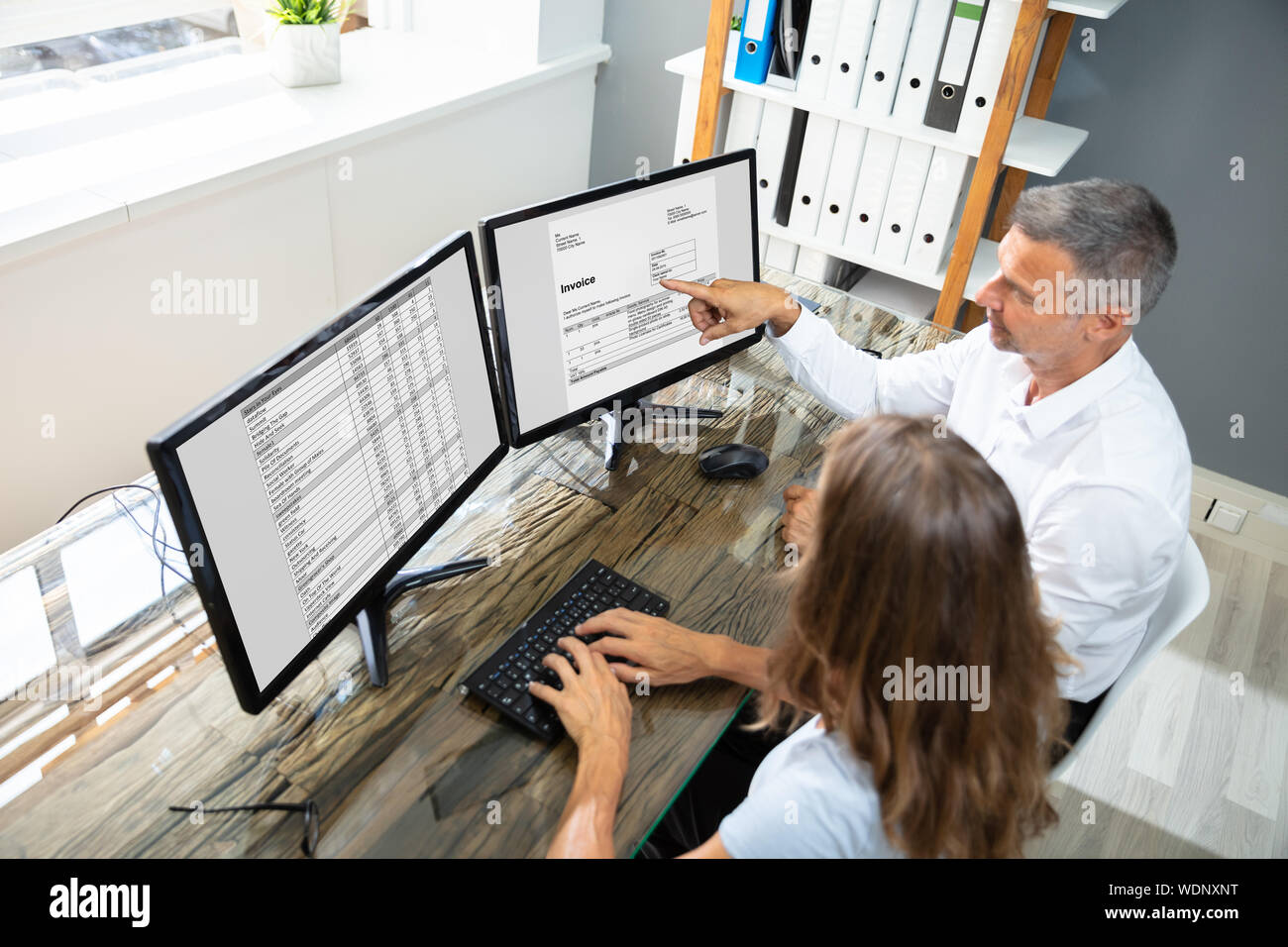 Side View Of Two Businesspeople Checking Invoice On Computer Over Desk