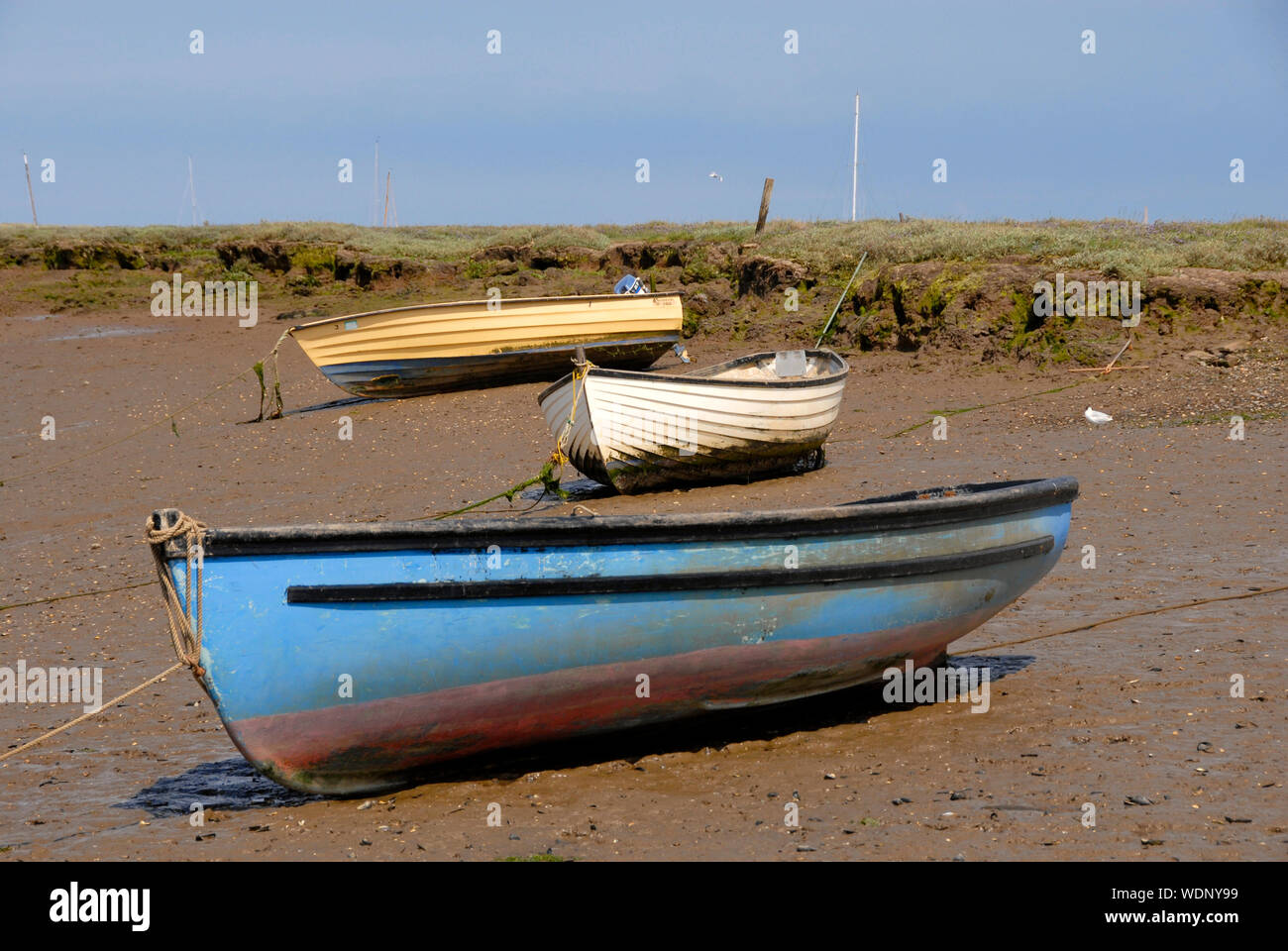 Three boats on the mud at low tide at Brancaster Staithe, Norfolk, England Stock Photo