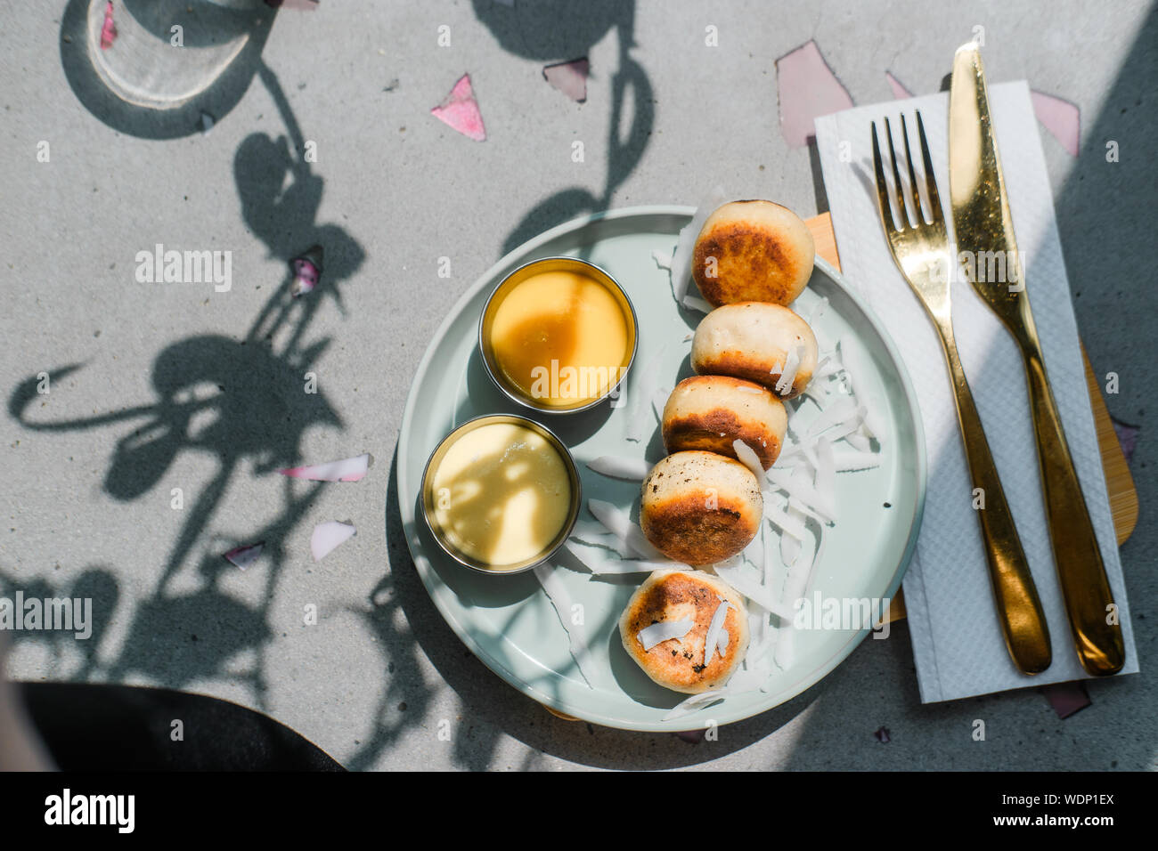 Vegan tofu cheese pancakes on blue plate, gray concrete table. Direct sun light, focus on shadows. Food blog photography concept. Overhead Stock Photo