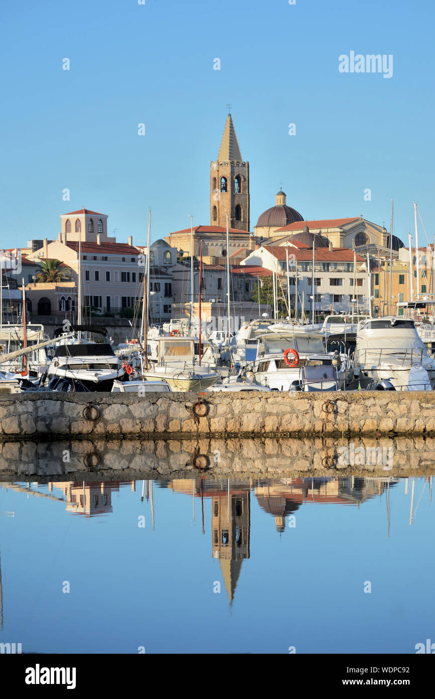 panoramic view of alghero with the bell tower of the cathedral in evidence and its reflection on the water of the port Stock Photo