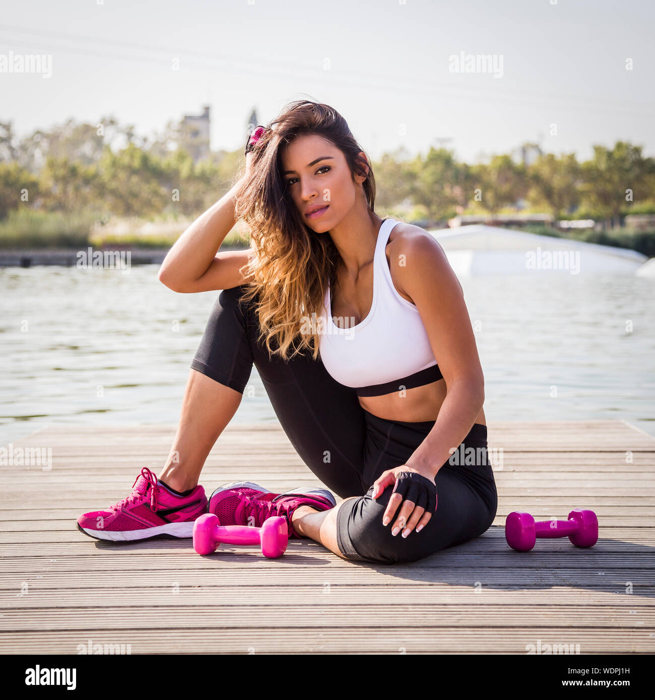 Young Woman In Sports Clothing Sitting By Lake Stock Photo