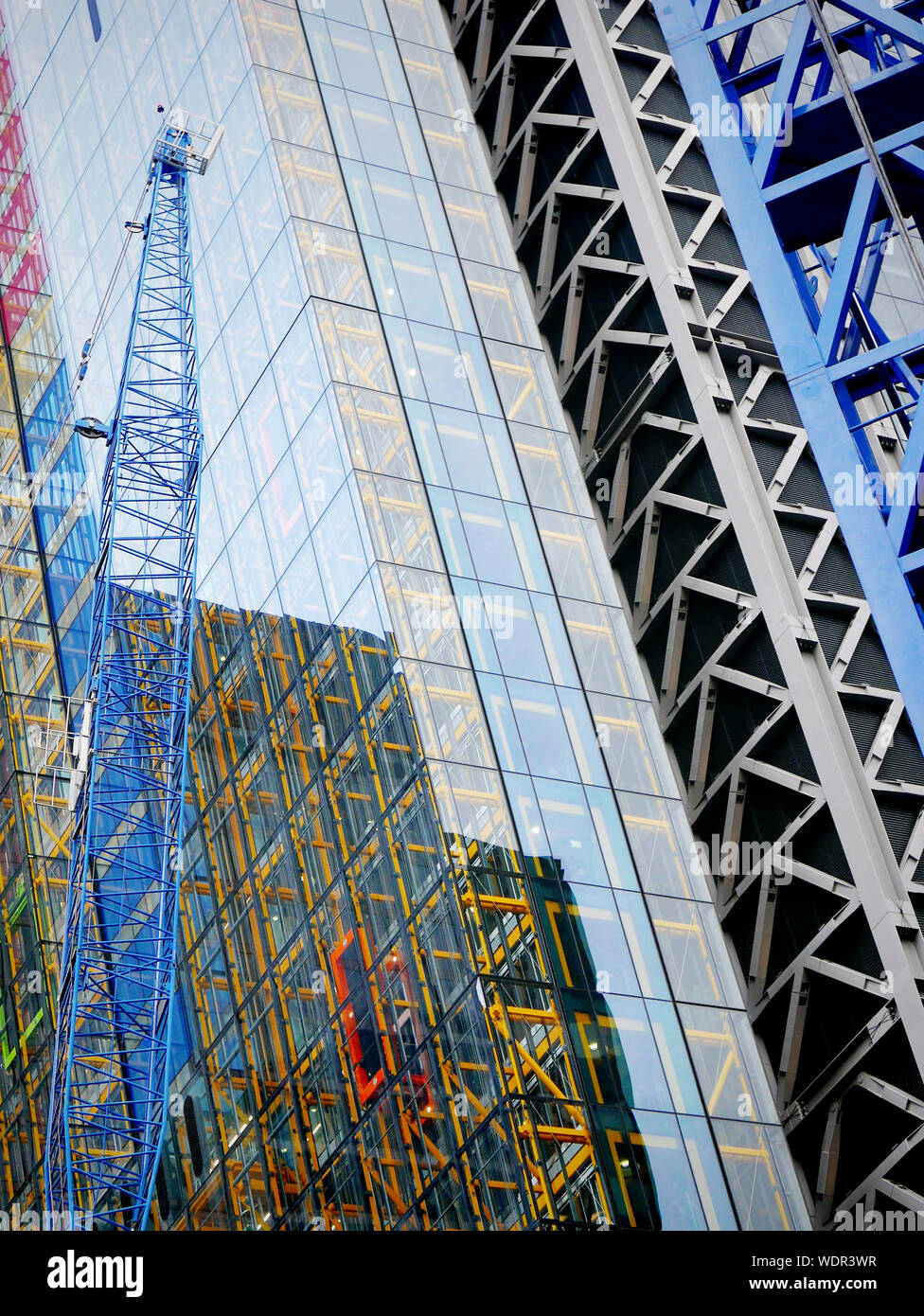 Low Angle View Of Crane By Glass Building At Construction Site Stock Photo