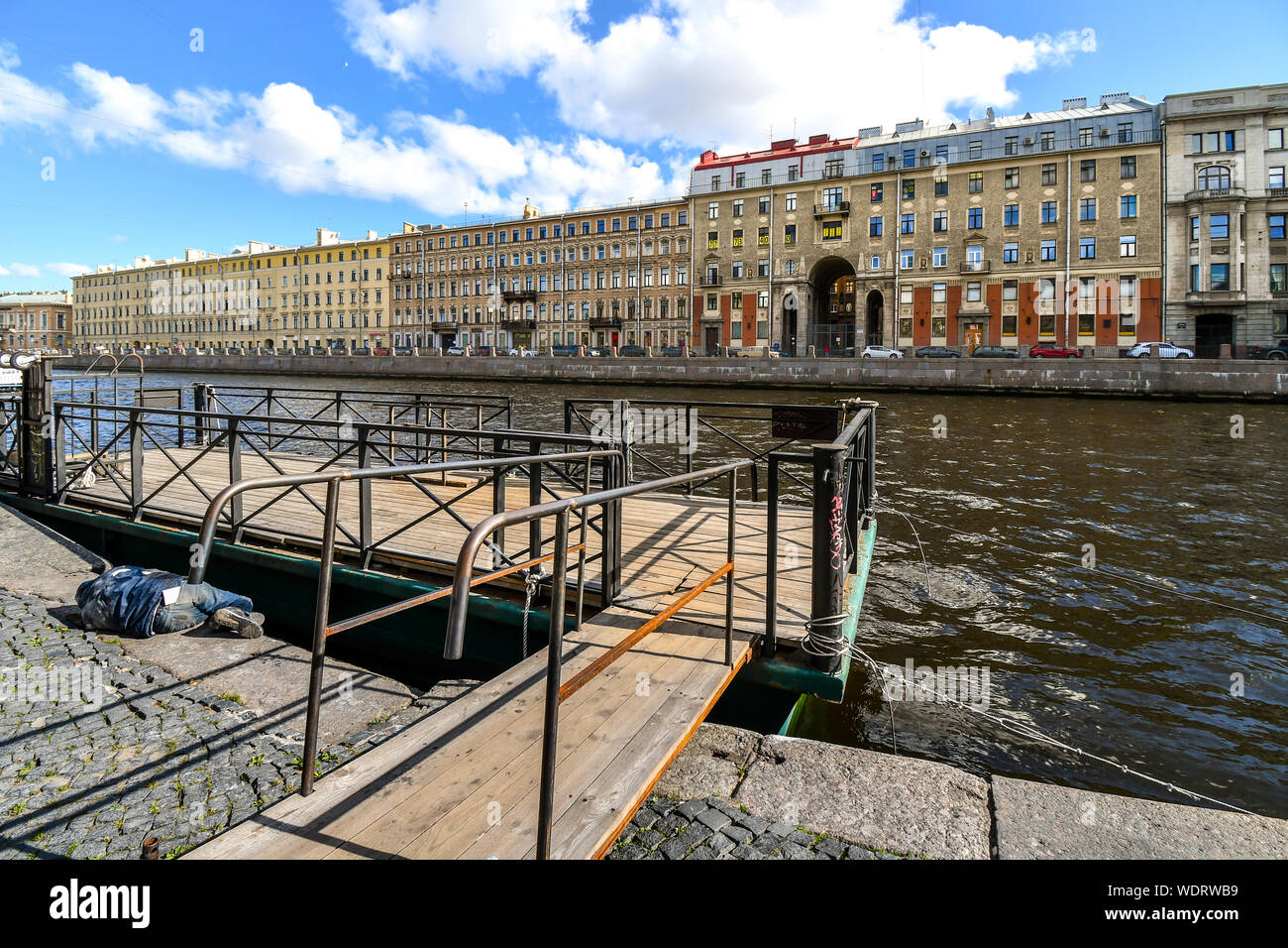 A homeless man sleeps on a sidewalk near a boat dock on the Neva River in historic St. Petersburg, Russia Stock Photo
