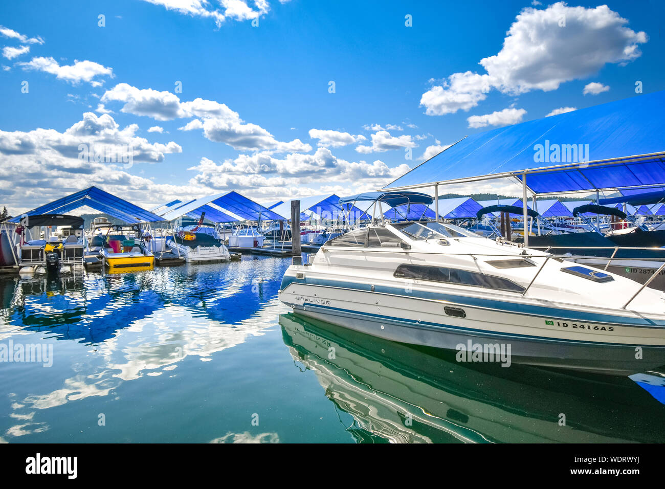 An expensive luxury speedboat sits near covered boat slips filled with boats on the floating boardwalk of the Coeur d'Alene Resort Stock Photo