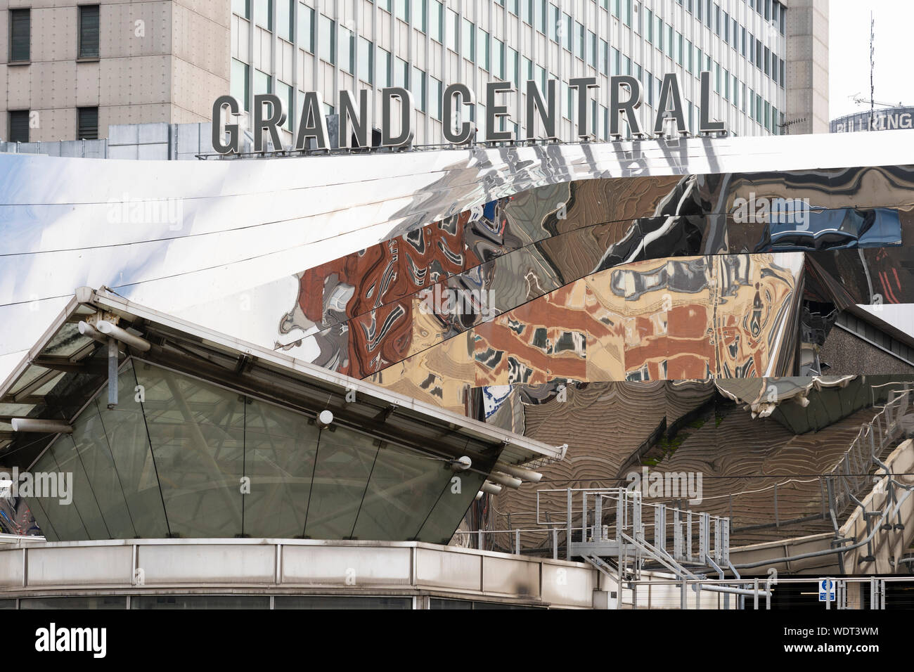 The modern stainless steel facade of Grand Central shopping centre in Birmingham contrasts with the 1960s Birmingham New Street station below Stock Photo