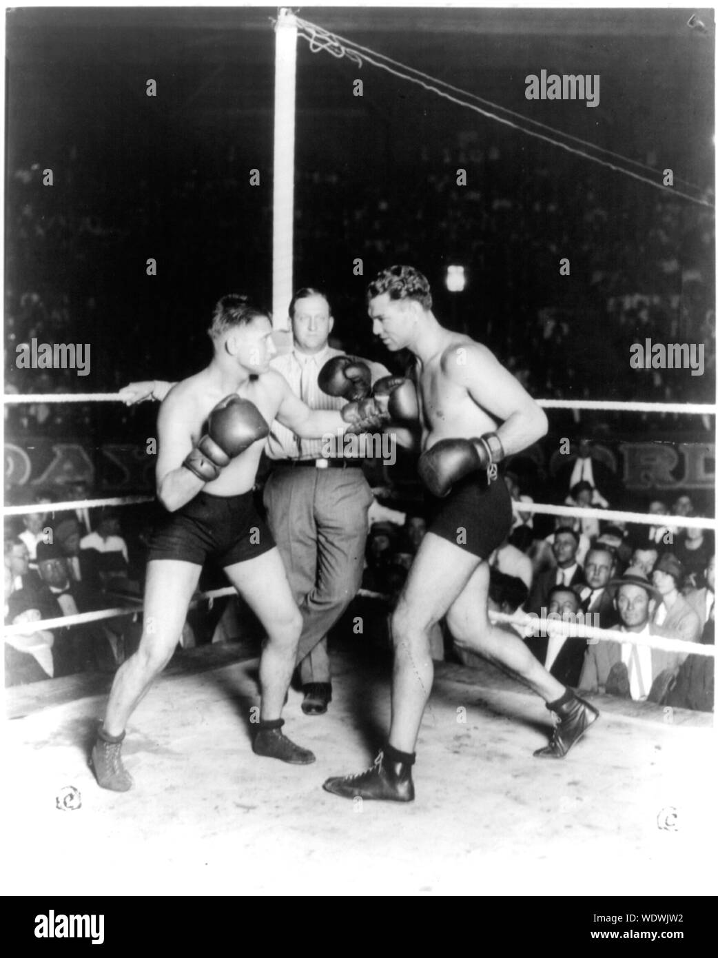 Gus Wilson, Jack Dempsey, Ray Newman, San Antonio, Tex., Sept. 25, 1925 Photograph shows Jack Dempsey preparing to exchange punches with Gus Wilson in boxing ring in front of large crowd referee, Ray Newman, leaning against ropes watches. Stock Photo