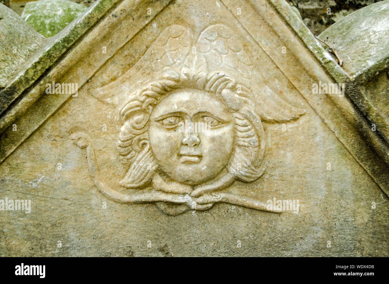An ancient carving of an angel with a chubby face and what looks like a snake around its neck and wings behind.  Stone sarcophagus dating from late Ro Stock Photo