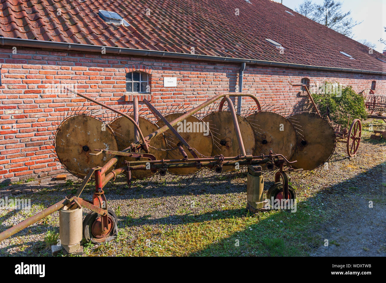 Wide angle view of an old, rusty tedder on a brick barn. Stock Photo