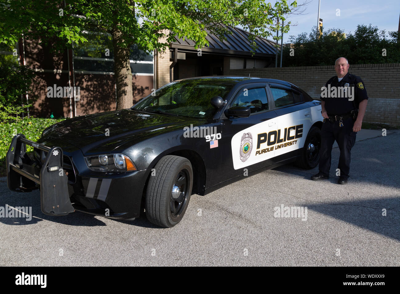 A uniformed police officer stands next to a 2011 Dodge Charger squad car outside the Purdue University Police Department in Fort Wayne, Indiana, USA. Stock Photo