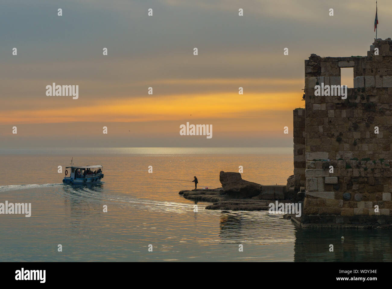A man fishing near a tourist boat at sunset in Byblos harbour Lebanon 5 february 2018 Stock Photo
