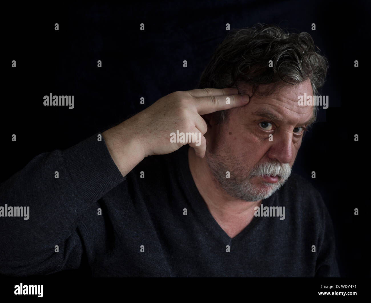 Portrait Of Mature Man Shooting Himself Against Black Background Stock Photo