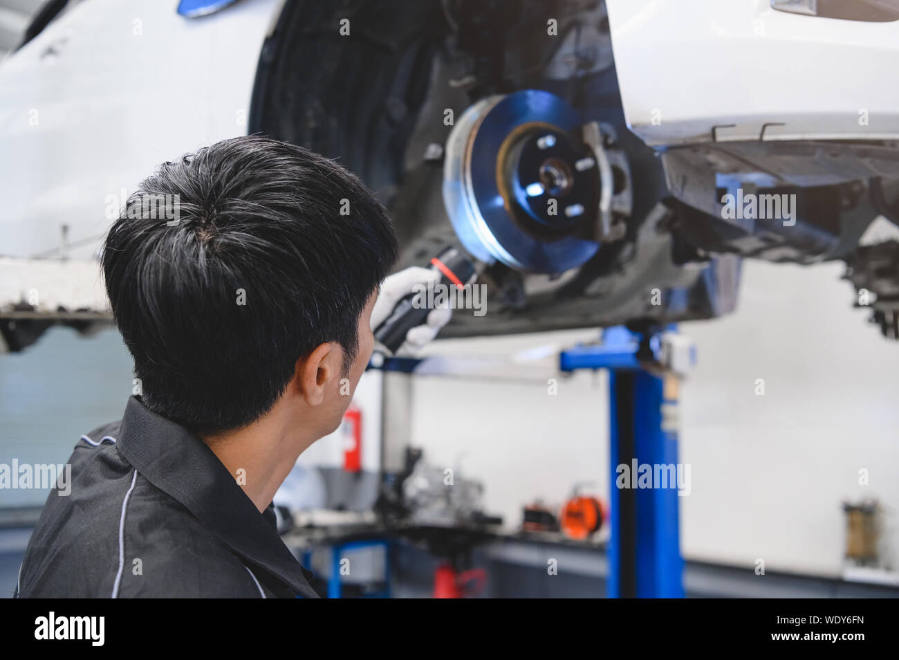 Asian male mechanical hold and shining flashlight to examine car disk