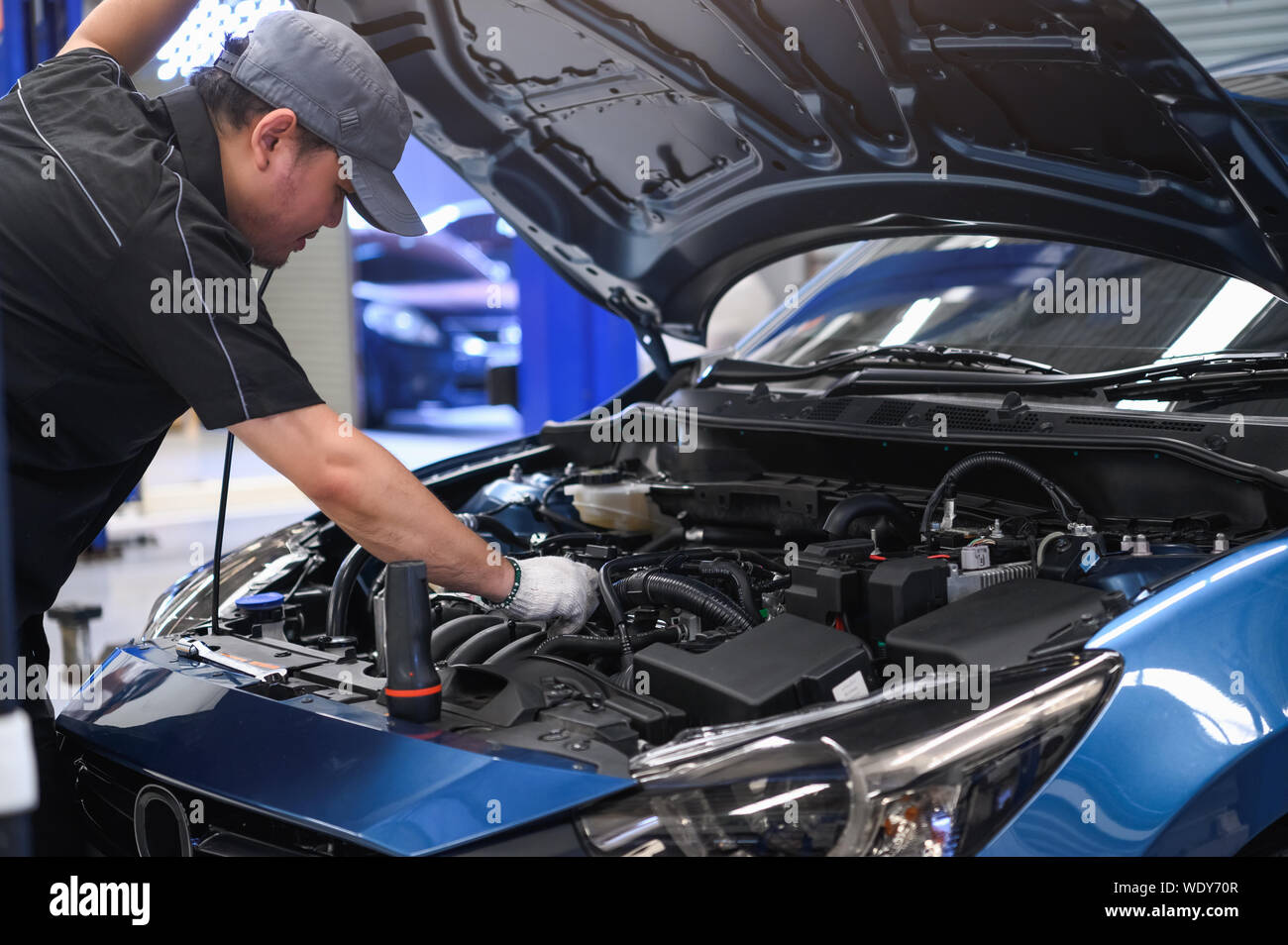 Asian male auto mechanic examine car engine breakdown problem in front