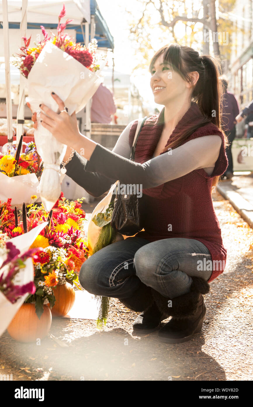 Happy, smilling, young Hispanic woman shopping for fresh flowers at farmers market. City living weekend lifestyles. Stock Photo