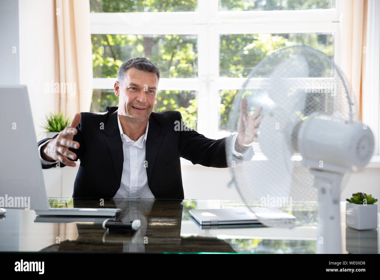 Businessman Sitting Near Fan In Office During Hot Weather Stock Photo