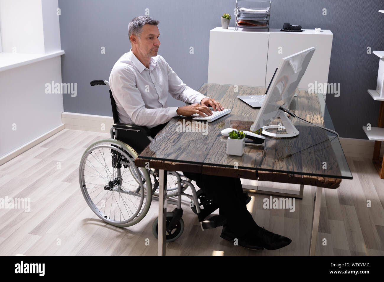 Handicapped Businessman Sitting On Wheelchair And Using Computer In
