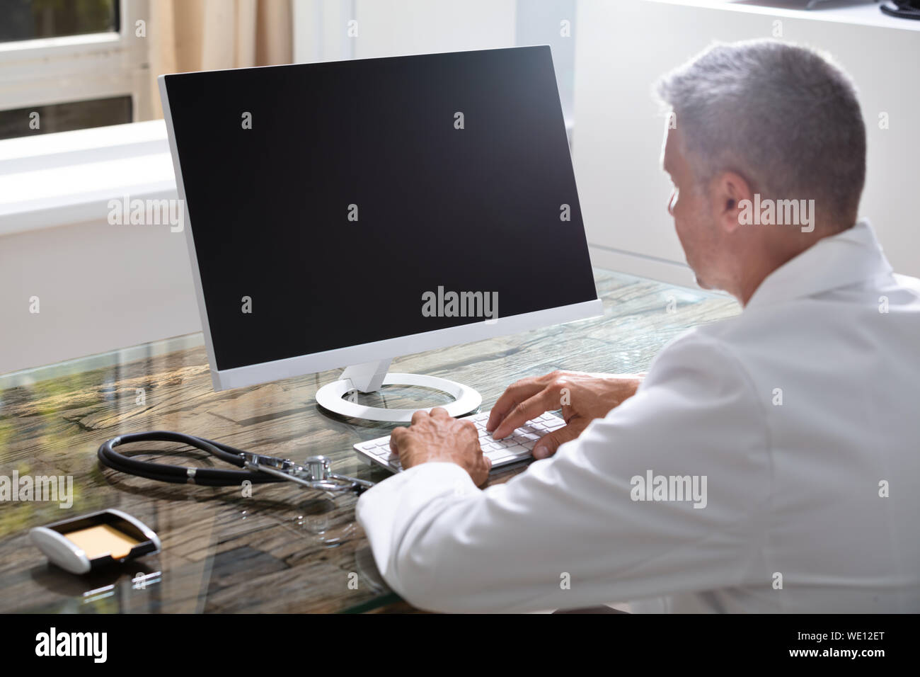 Confident Male Doctor Working On Computer At Desk Stock Photo