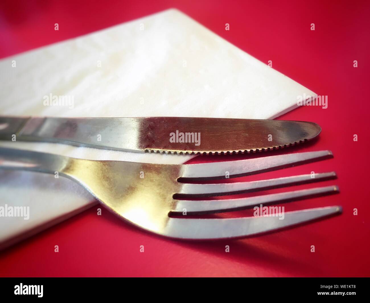 Close-up Of Cutlery With Serviette On Red Table Stock Photo