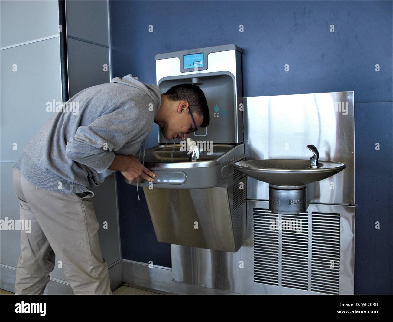 A BOY DRINKS WATER FROM A SMALL FOUNTAIN INSIDE JFK AIRPORT IN NEW YORK