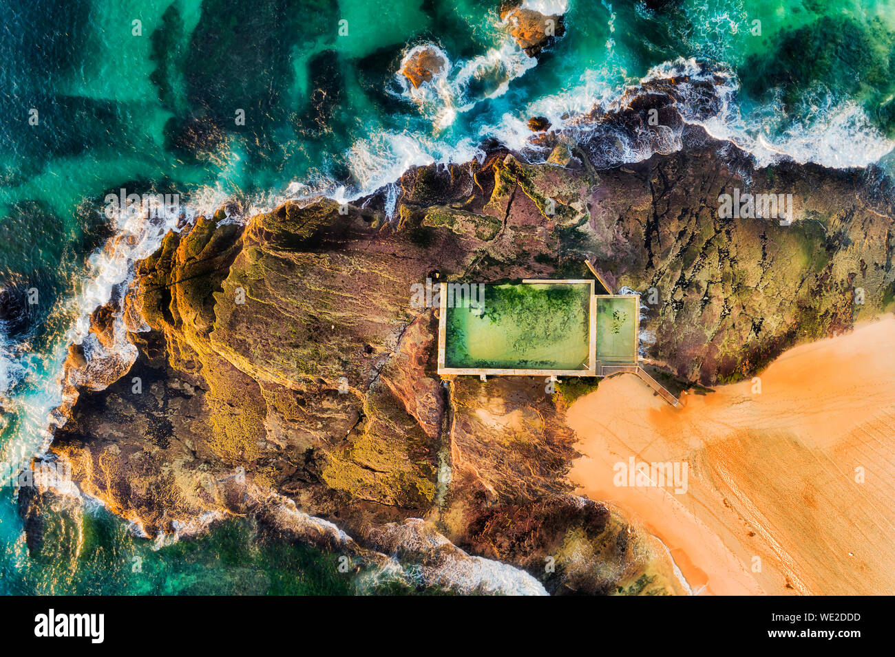 Rectangular swimming rock pool on Mona Vale beach sandstone plateau on a surf line of Pacific ocean waves in aerial top down view in soft morning ligh Stock Photo
