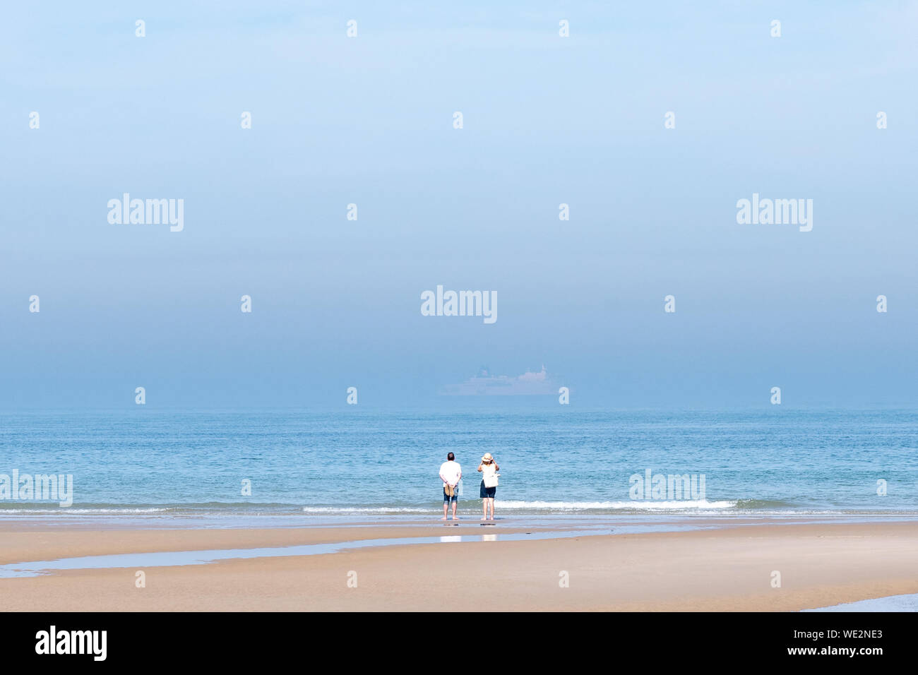 2 people looking at a boat in the mist across the English channel Stock Photo