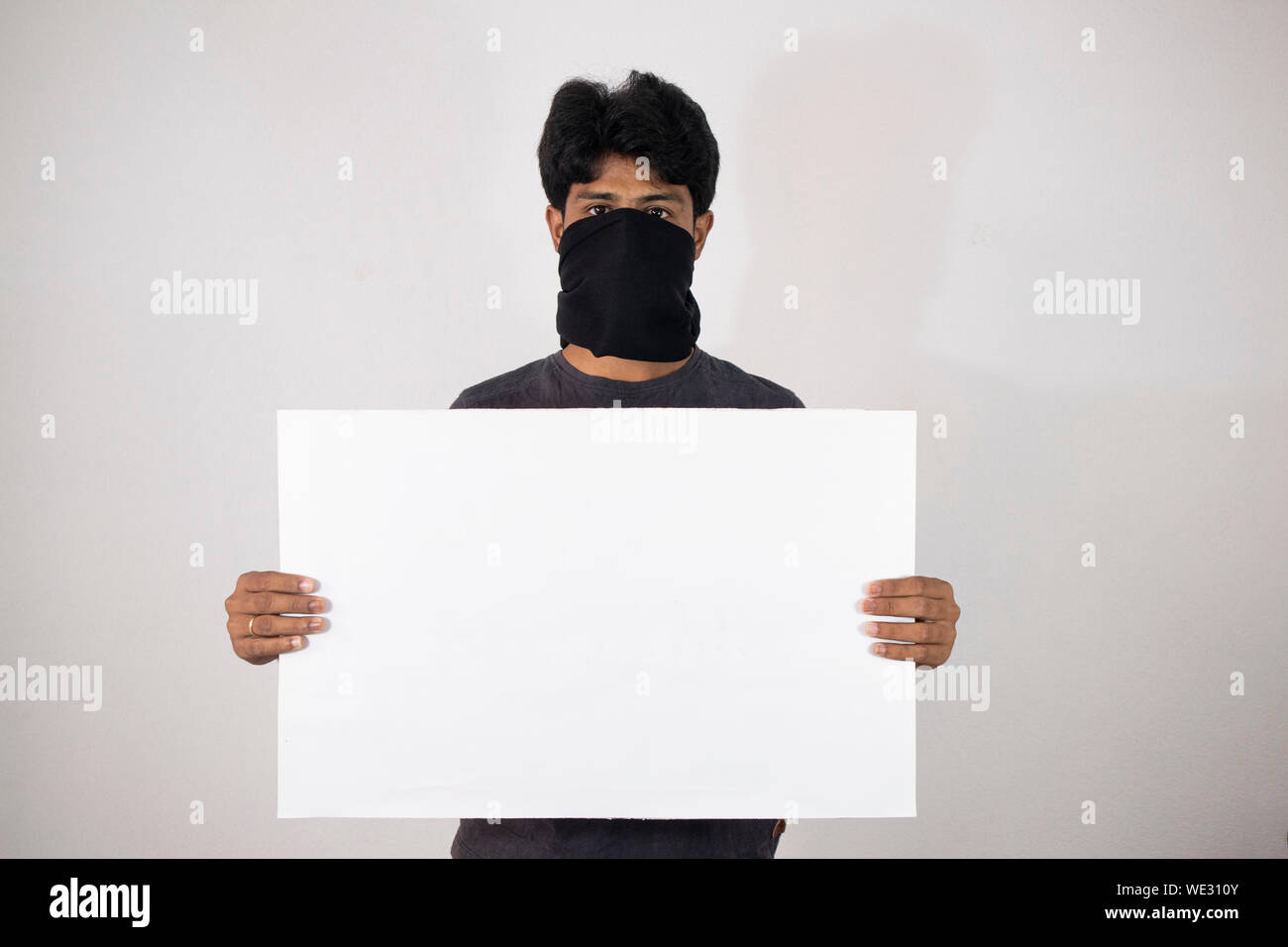 Concept of protest showing with Man standing by covering the face with black cloth and holding Empty banner, placard on isloated background. Stock Photo