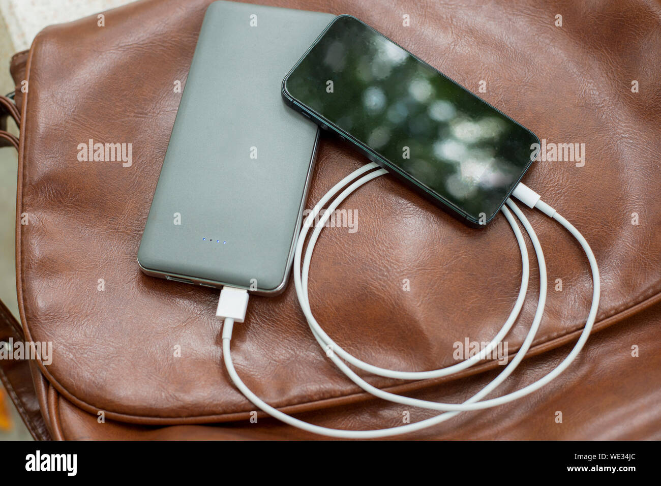 High Angle View Of Mobile With Portable Charger On Brown Leather Bag Stock Photo
