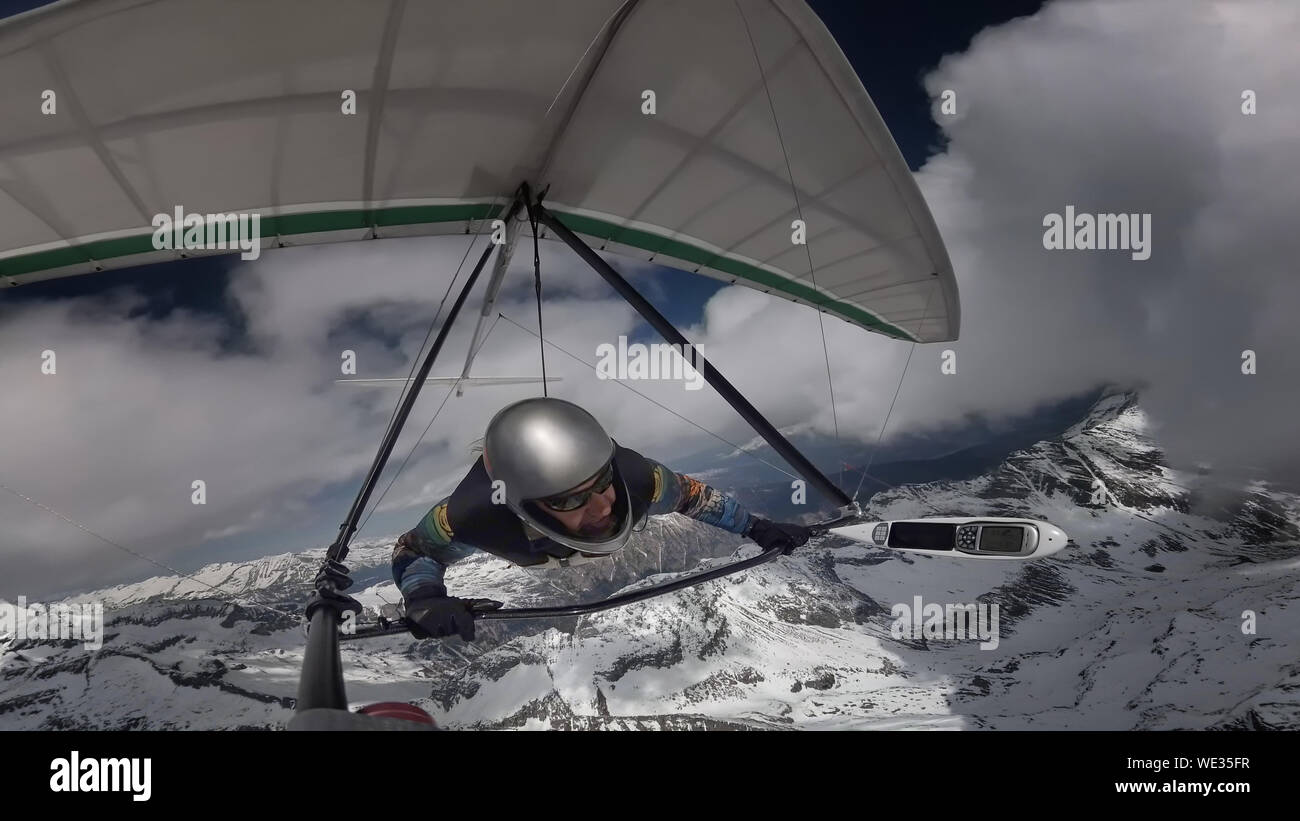 Hang glider pilot fly with his wing on high altitude between clouds above snow mountain peaks. Extreme sport. Stock Photo
