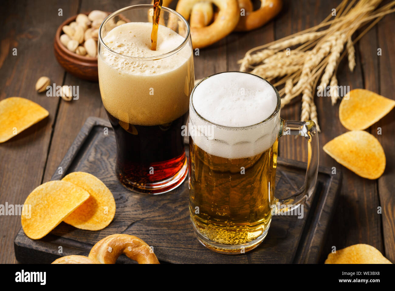 Light and dark beer with various snacks - chips, pretzels and nuts on a dark wooden background. Stock Photo