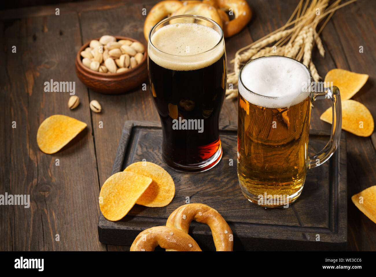 Light and dark beer with various snacks - chips, pretzels and nuts on a dark wooden background. Copy space. Stock Photo