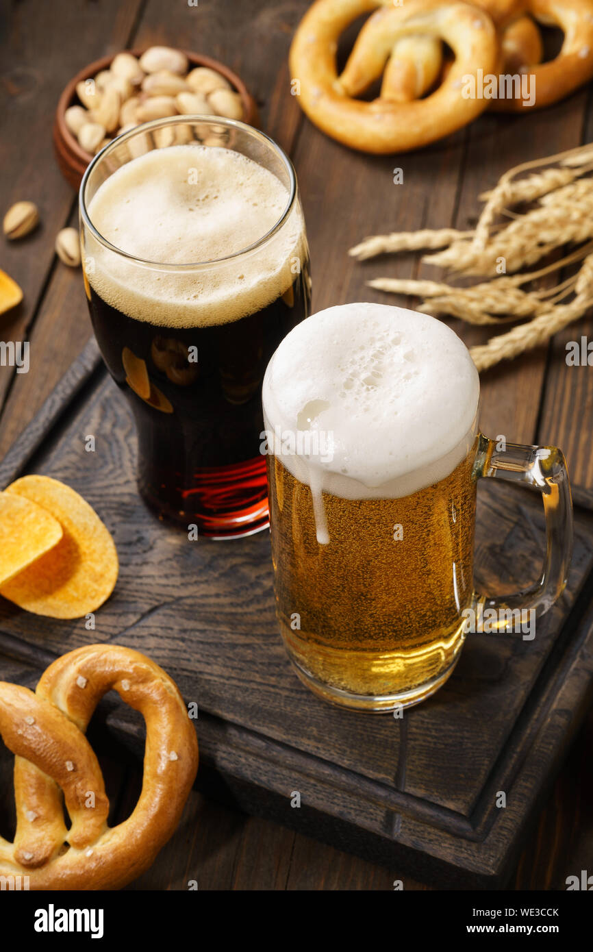 Light and dark beer with various snacks - chips, pretzels and nuts on a dark wooden background. Stock Photo