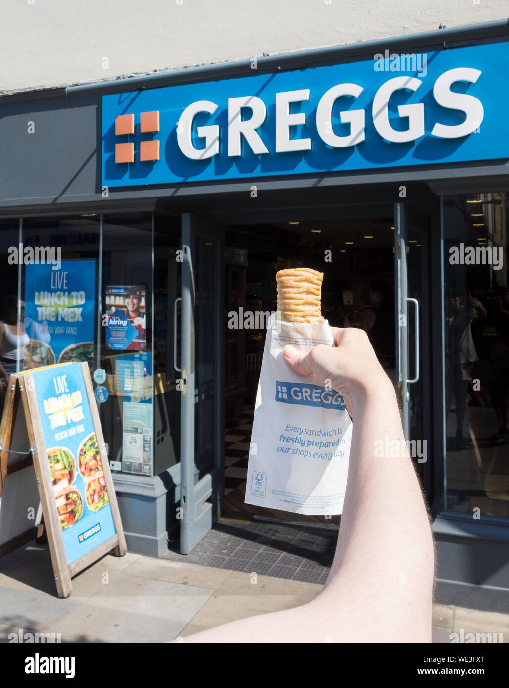 A young woman clutching a Greggs vegan-friendly sausage roll outside a Greggs in Richmond, Surrey, UK Stock Photo