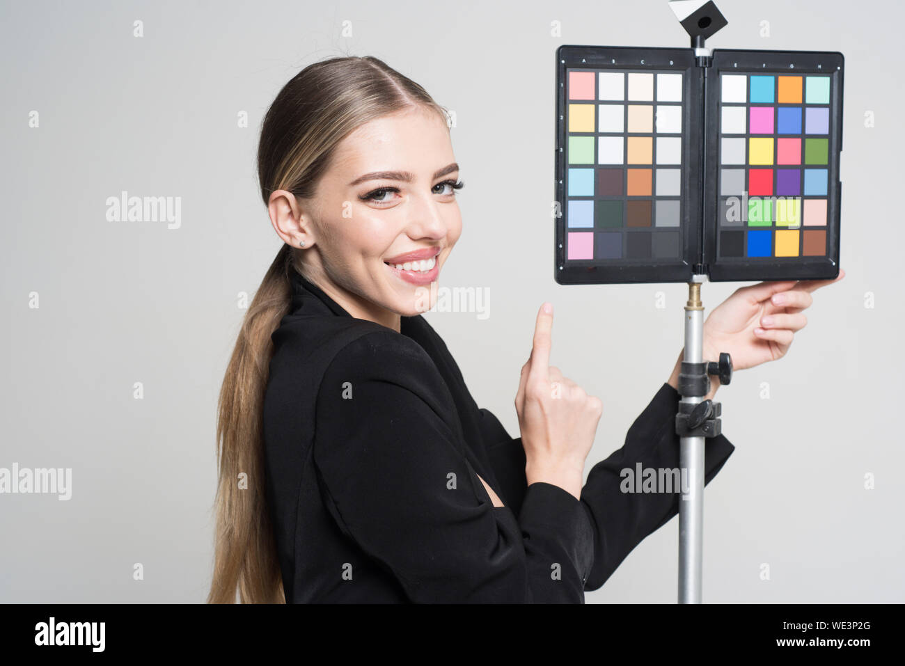 Young photographer pointing at color checker card, while working in studio. Girl in formal suit prepares for photo shooting. Photography concept. Woma Stock Photo